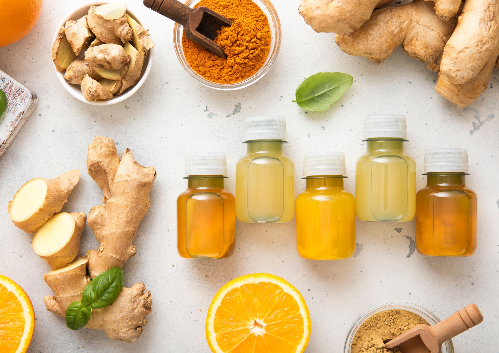 Bottles of immune turmeric ginger energy shot drink with fresh raw ginger roots and oranges fruits on light background.Top view.